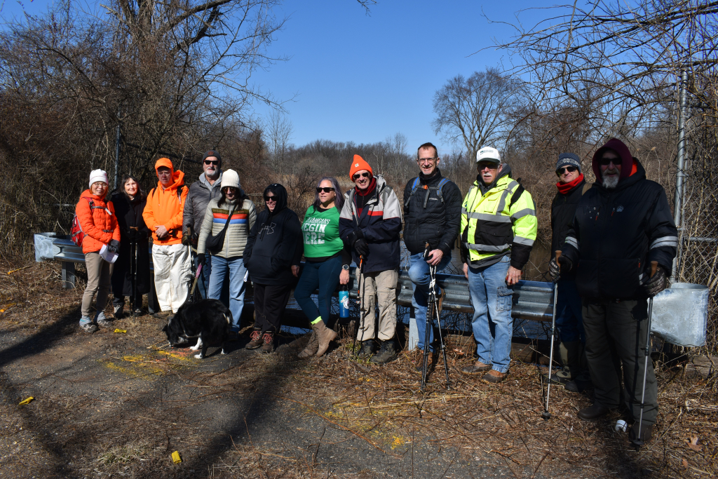 Group of people posing for a photo during an eco tour on a trail, dressed warmly with a dog in front.