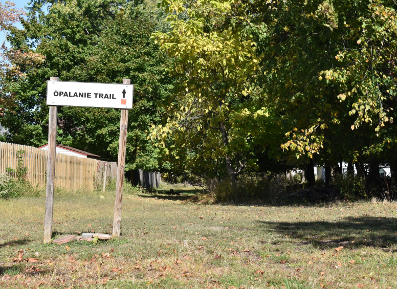 “Opalanie Trail” sign marking the grassy trail entrance near a wooden fence.