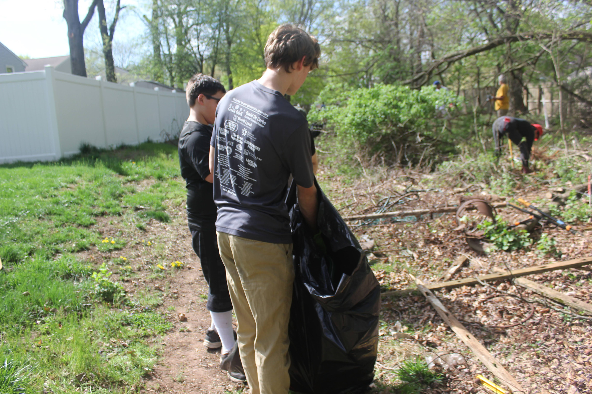 Scouts placing branches and debris into a trash bag along a fence.