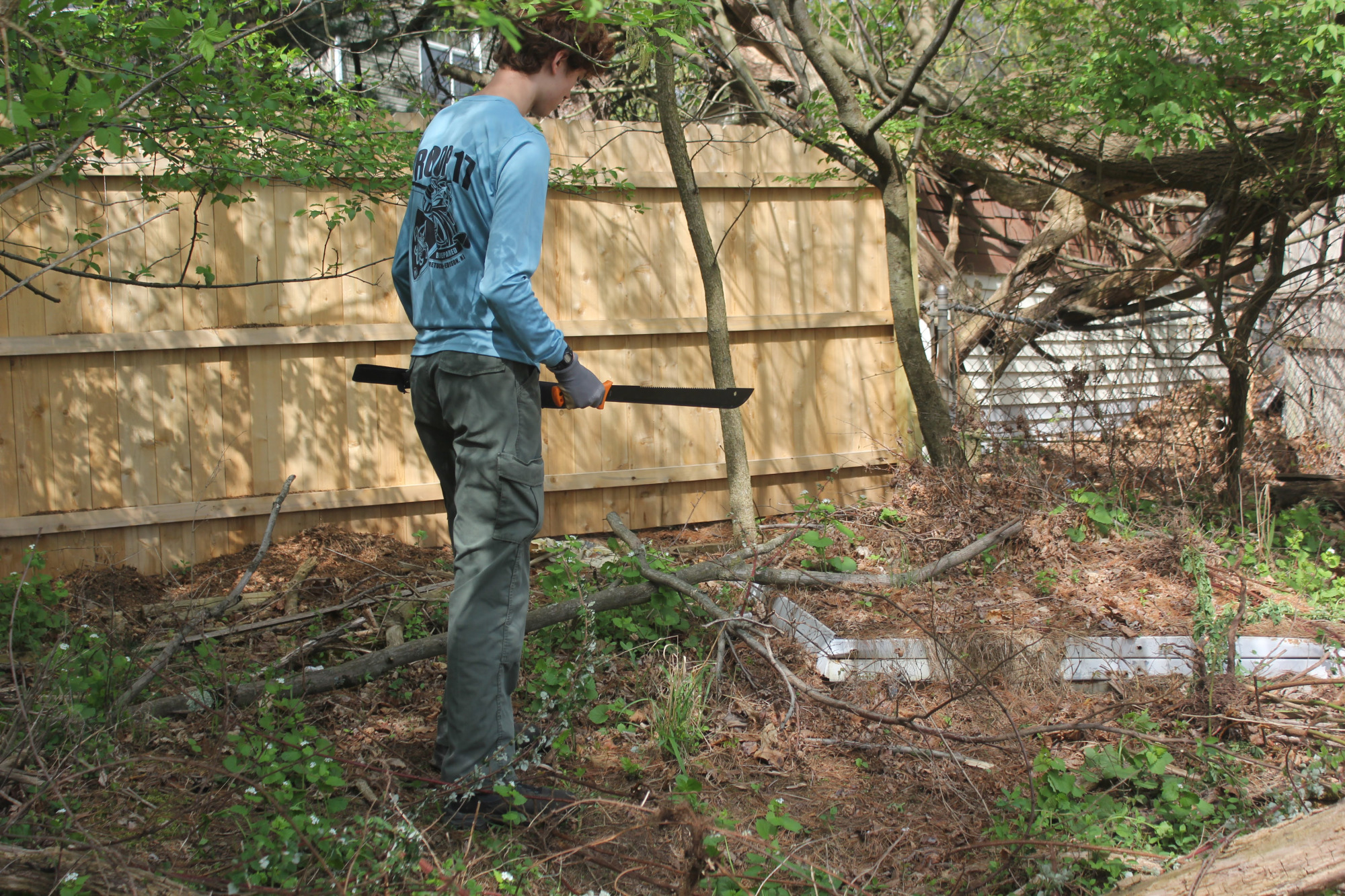 Scout cleaning up debris near a wooden fence in a wooded area.