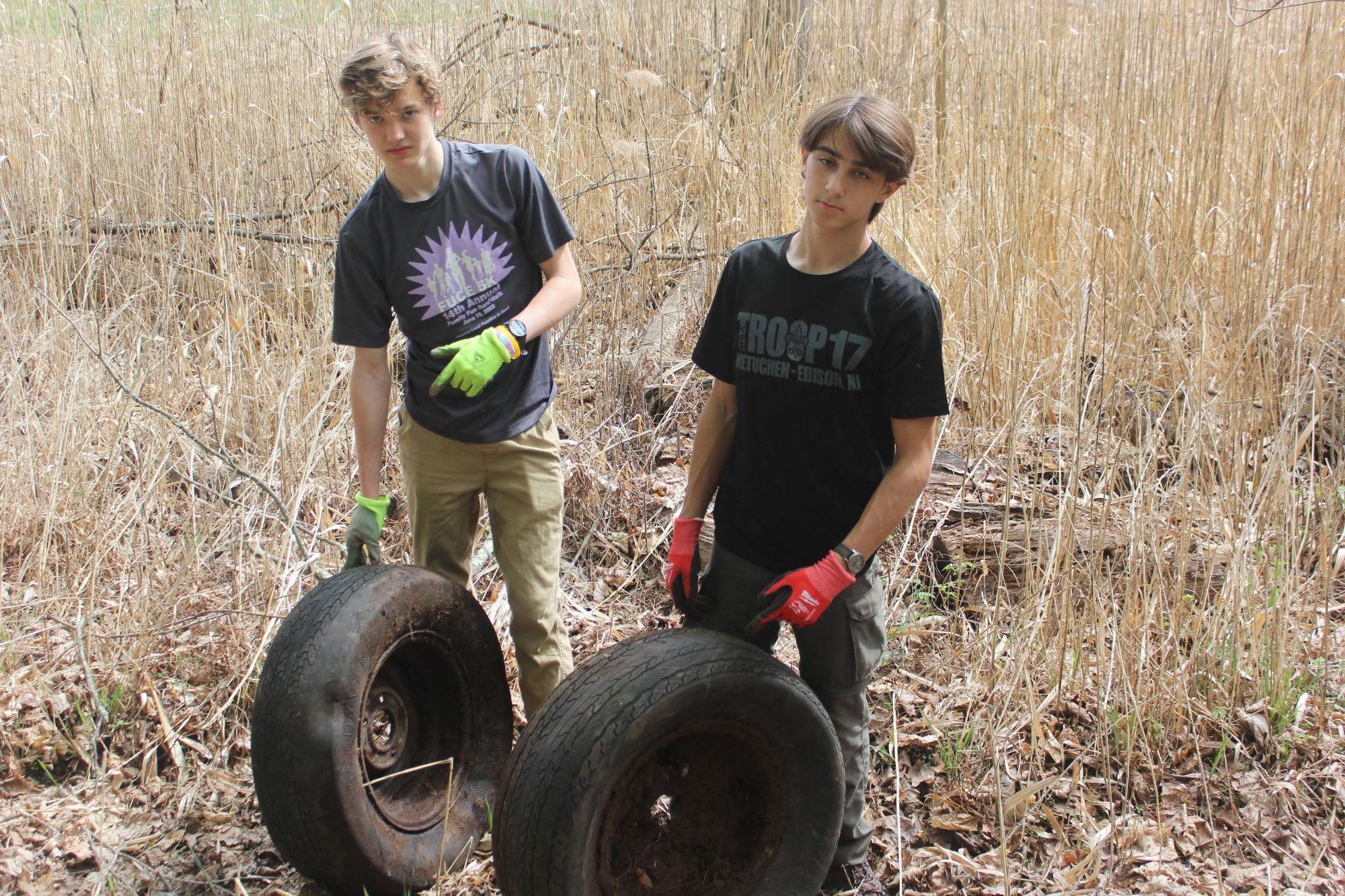 Two scouts holding up two large tires in a field of dry reeds.