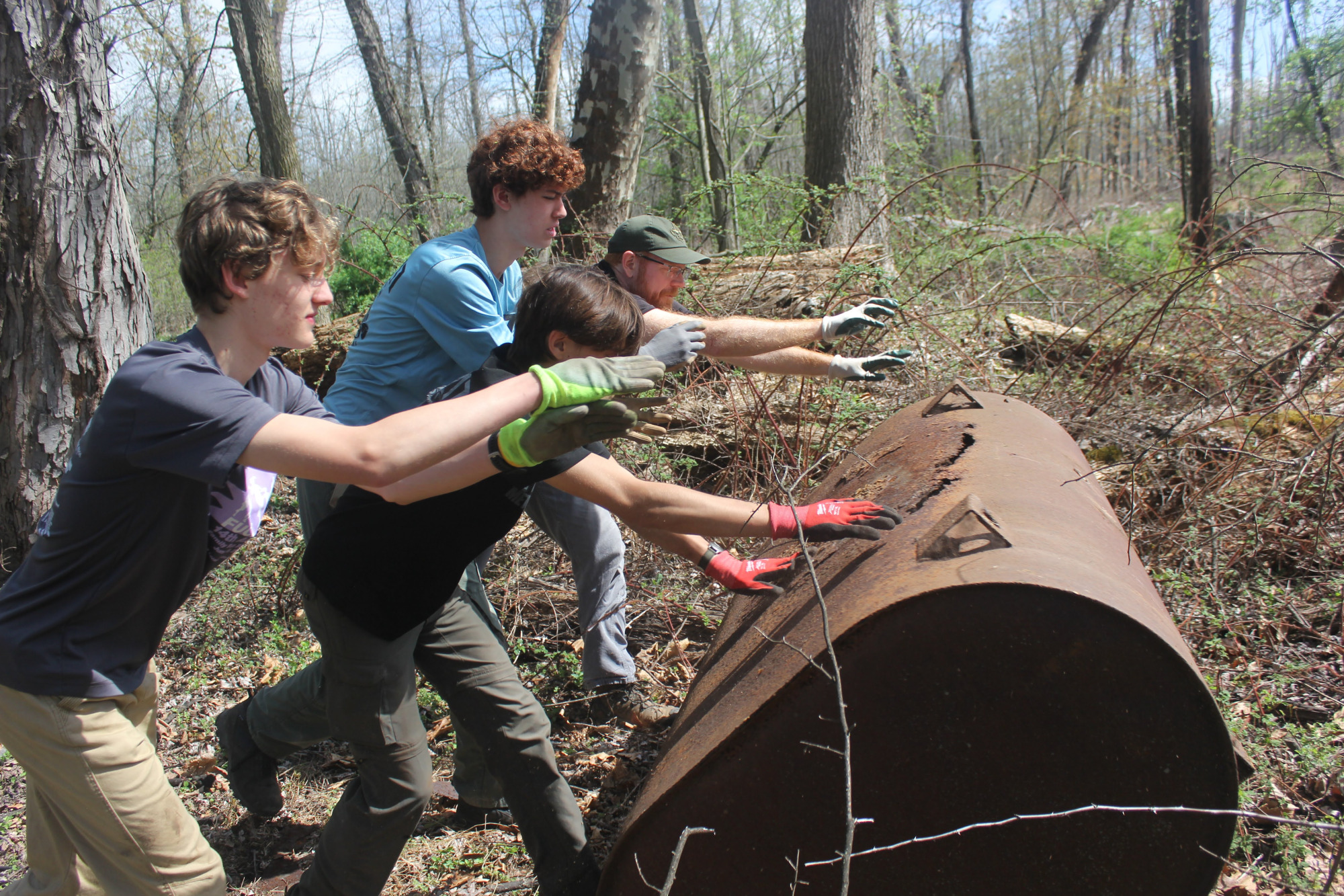 Scouts using tools to remove vines and debris from a rusted tank.