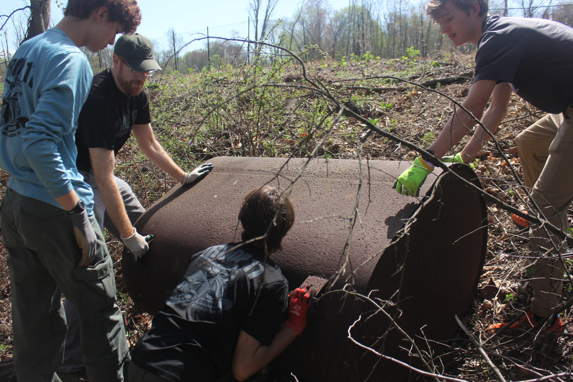 Scouts lifting a rusted tank partially buried in brush.