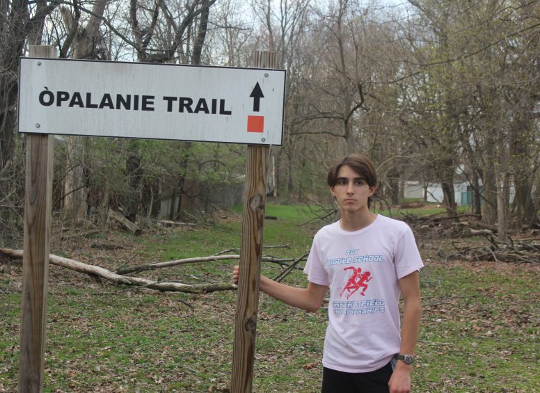 Young man standing beside the “Opalanie Trail” sign at the wooded trailhead.