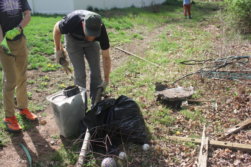 Volunteers lifting a heavy object into a trash bag on the ground.