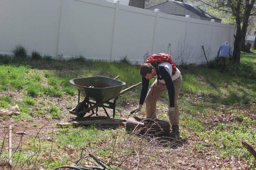 Volunteer using a wheelbarrow to collect debris from the ground.