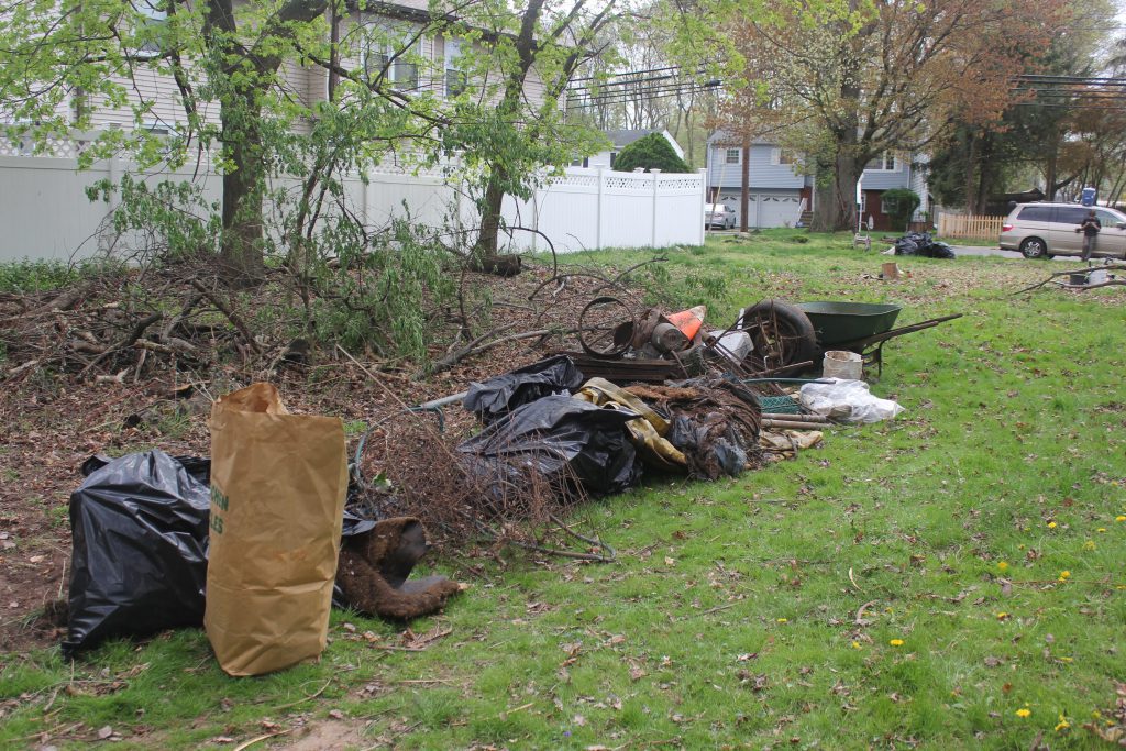 Large pile of trash bags, scrap metal, and yard waste collected under trees.
