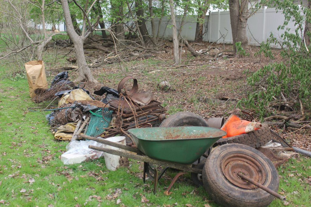 Wheelbarrow and tools next to a growing pile of yard waste and metal debris.