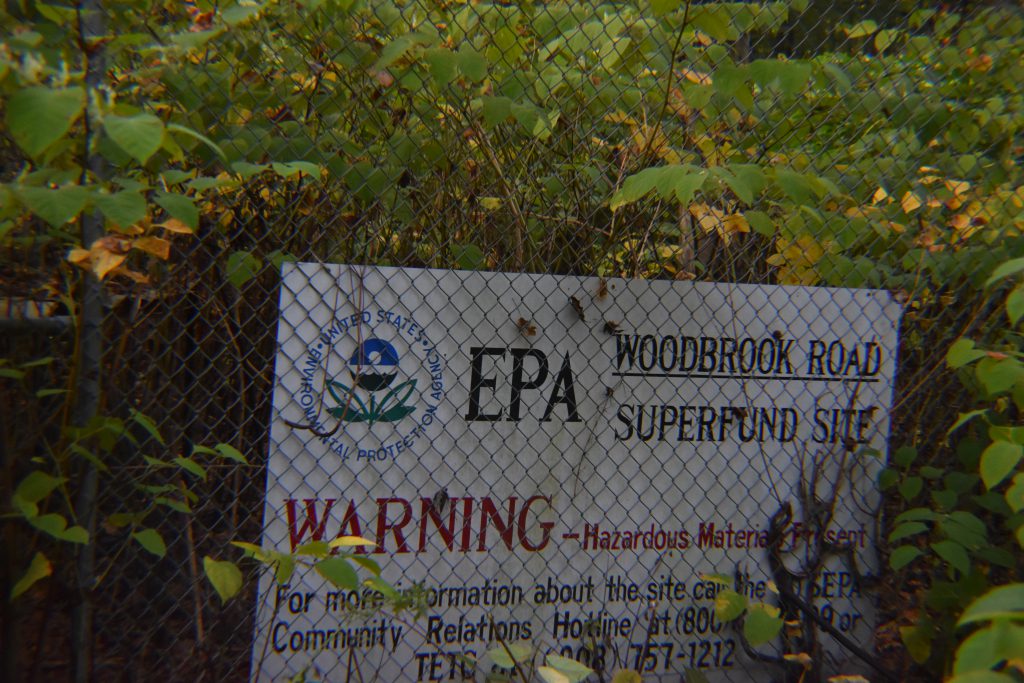 EPA warning sign on a chain-link fence indicating hazardous materials at the Woodbrook Road Superfund Site.