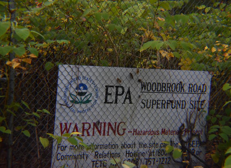 EPA warning sign on a chain-link fence indicating hazardous materials at the Woodbrook Road Superfund Site.